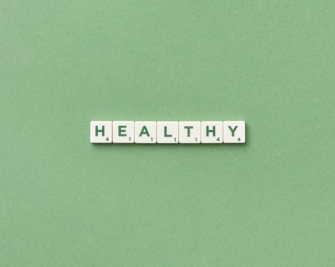 Scrabble tiles spelling the word 'healthy' on a light green background, top view.