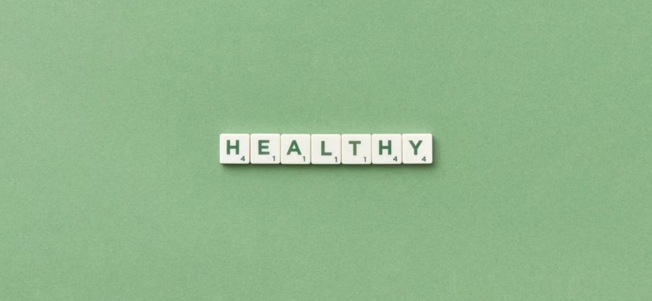 Scrabble tiles spelling the word 'healthy' on a light green background, top view.